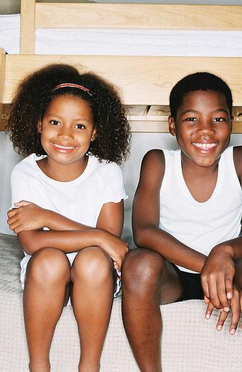 Siblings smiling together at the camera while wearing white clothing