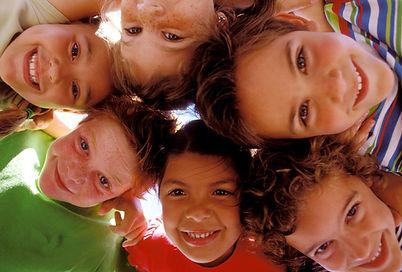 Group of children hugging in a circle and looking down at the camera