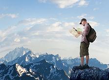 Young man standing on a mountain and looking at a map